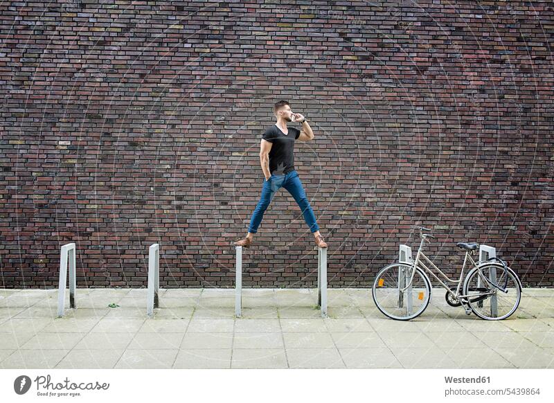 Man with cell phone balancing on bicycle rack in front of brick wall serious earnest Seriousness austere standing man men males mobile phone mobiles