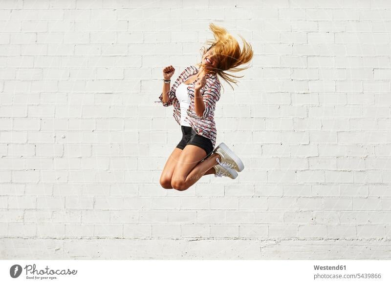 Happy young woman jumping mid-air in front of white wall females women Leaping Fun having fun funny happiness happy Adults grown-ups grownups adult people
