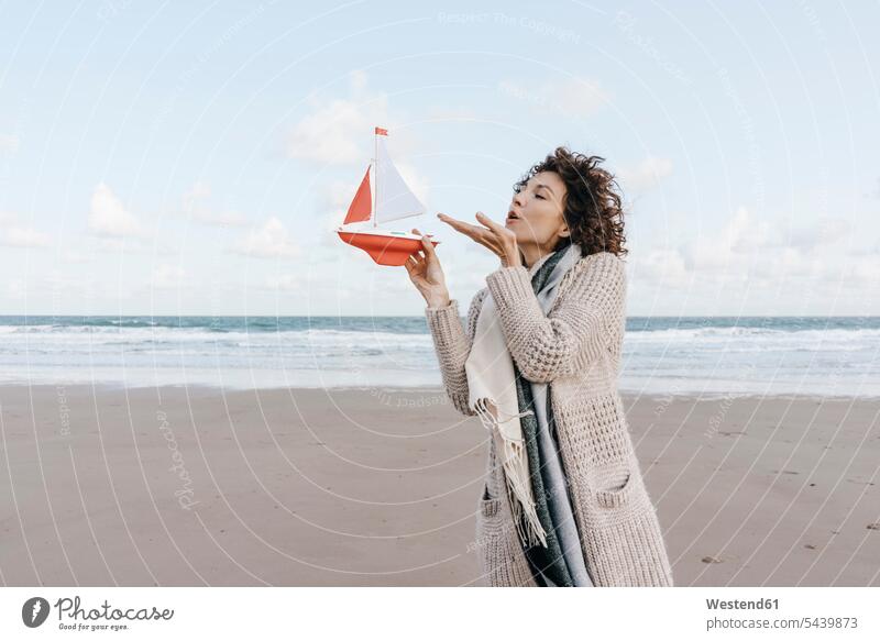 Woman blowing at toy boat on the beach portrait portraits woman females women beaches Adults grown-ups grownups adult people persons human being humans