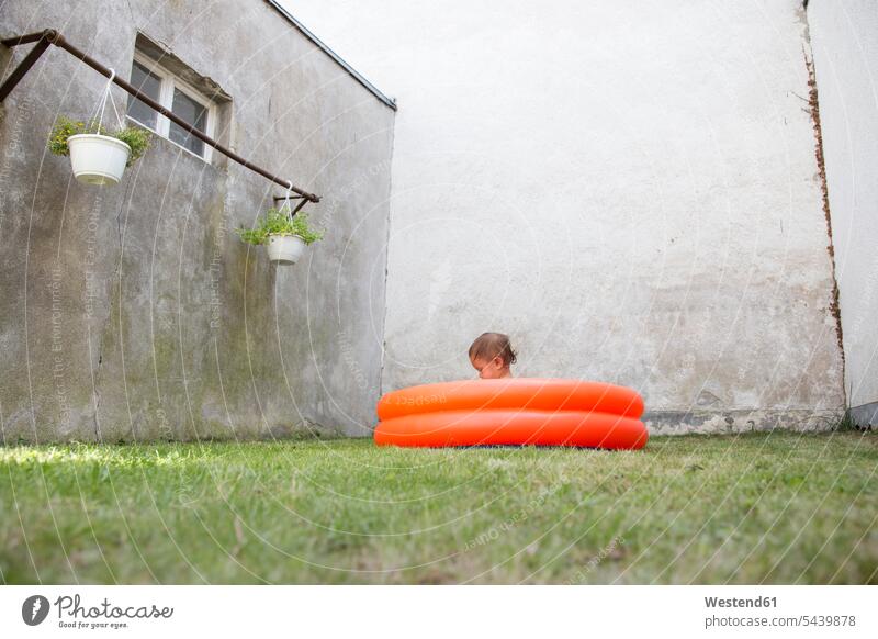 Germany, Freiburg, little girl sitting in a paddling pool at backyard playing childhood dull drabness backyards Facade Facades inflated grass Bright Colour