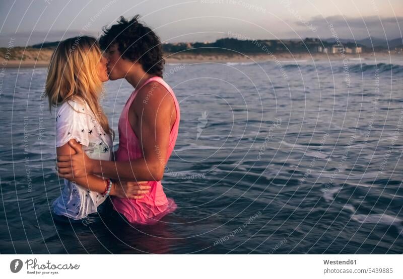 Young couple kissing in the sea at dusk ocean kisses twosomes partnership couples water waters body of water people persons human being humans human beings