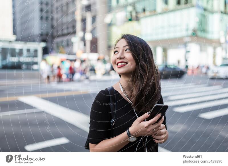USA, New York City, Manhattan, young woman listening music with cell phone and earphones on the street females women Adults grown-ups grownups adult people