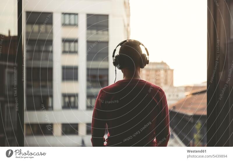 Man wearing headphones on a balcony in the city at sunset headset balconies standing man men males Adults grown-ups grownups adult people persons human being