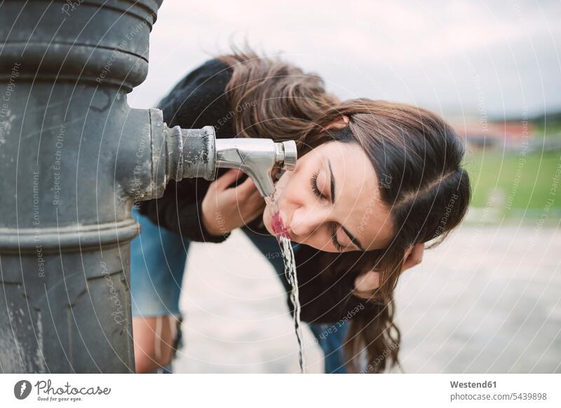 Young woman drinking water from a well females women Adults grown-ups grownups adult people persons human being humans human beings standing tap faucet taps