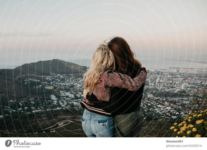South Africa, Cape Town, Kloof Nek, rear view of two women embracing at sunset girlfriend Girlfriends girl friend girl friends embrace Embracement hug hugging