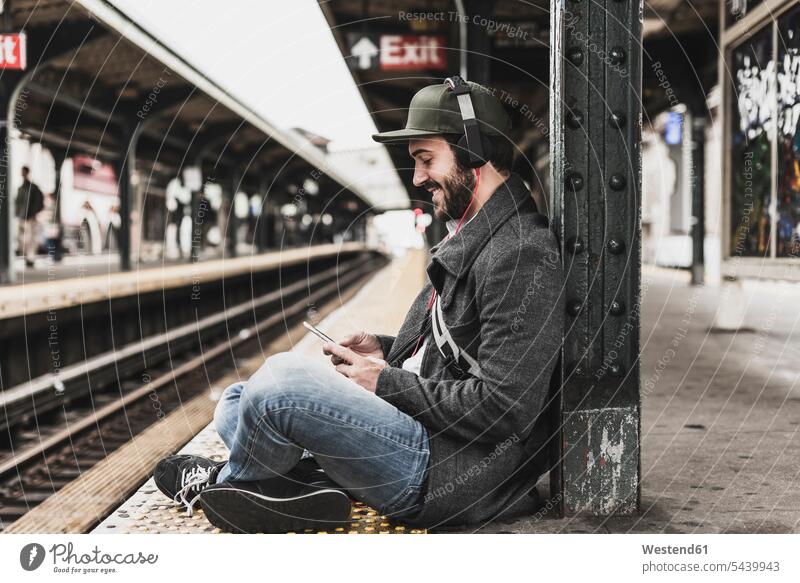 Young man waiting for metro at train station platform, using smart phone mobile phone mobiles mobile phones Cellphone cell phone cell phones music headphones