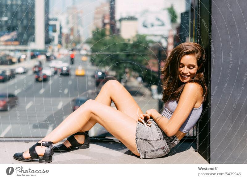 USA, New York City, smiling young woman relaxing in the city glass pane glass panes looking away look away relaxation relaxed beauty beautiful leaning top tops