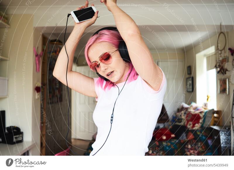 Enthusiastic young woman with pink hair listening to music at home glasses specs Eye Glasses spectacles Eyeglasses headphones headset females women hearing