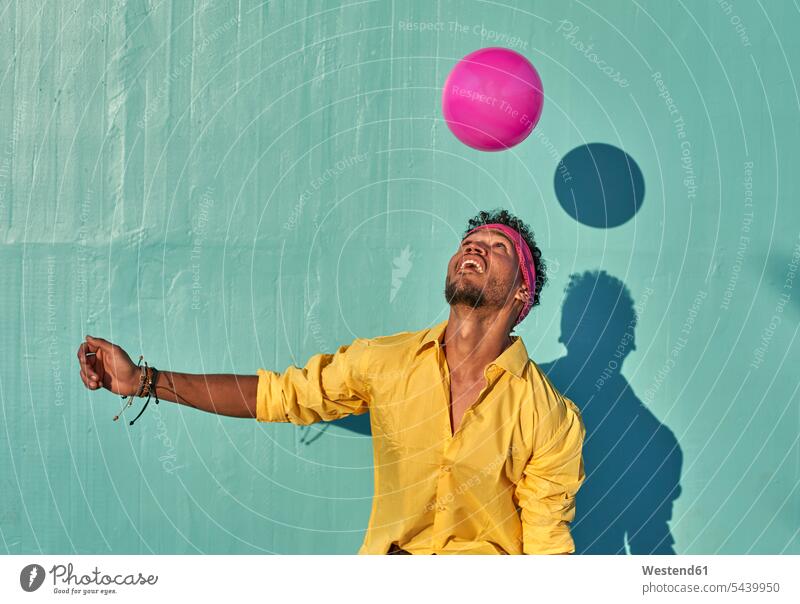 Young black man playing with a pink ball in front of a blue wall shirts balls delight enjoyment Pleasant pleasure happy Emotions Feeling Feelings Sentiment