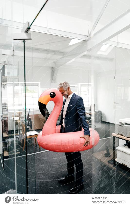 Happy businessman in office with inflatable flamingo Businessman Business man Businessmen Business men offices office room office rooms laughing Laughter