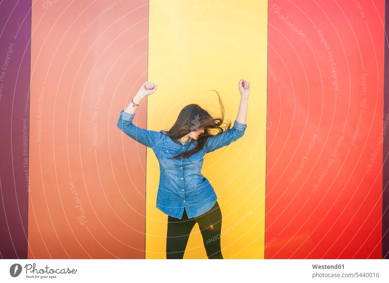 Happy young woman dancing in front of colourful wall females women dance Adults grown-ups grownups adult people persons human being humans human beings standing