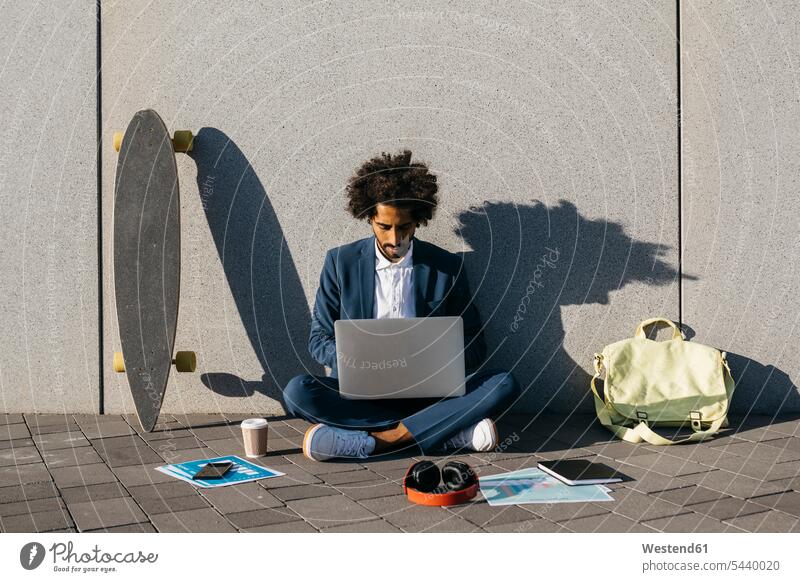 Young businessman sitting outdoors at a wall working on laptop Seated Businessman Business man Businessmen Business men At Work Laptop Computers laptops