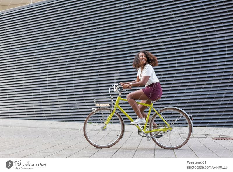 Smiling young woman riding bicycle riding bike bike riding cycling bicycling pedaling bikes bicycles smiling smile females women transportation Adults grown-ups