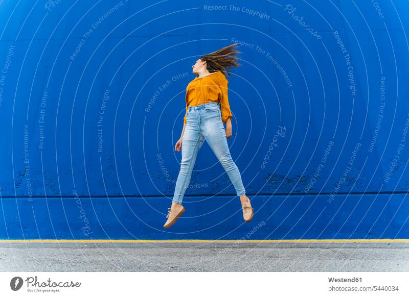 Young woman jumping in front of a blue wall human human being human beings humans person persons adult grown-up grown-ups grownup grownups young young adult
