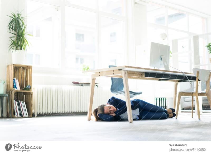 Businesswoman lying under the table in office sleeping businesswoman businesswomen business woman business women females asleep laying down lie lying down
