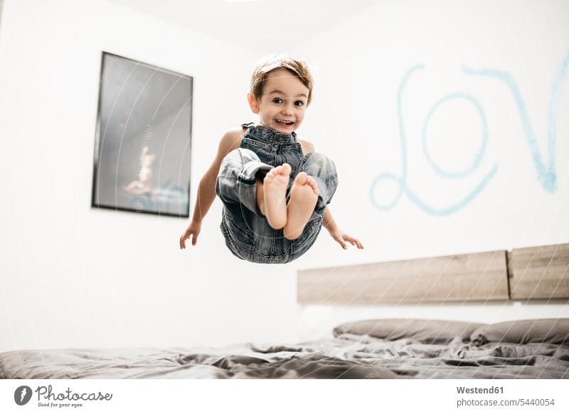 Happy little boy jumping on the bed jump in the air jumping in the air beds boys males Leaping jumps child children kid kids people persons human being humans