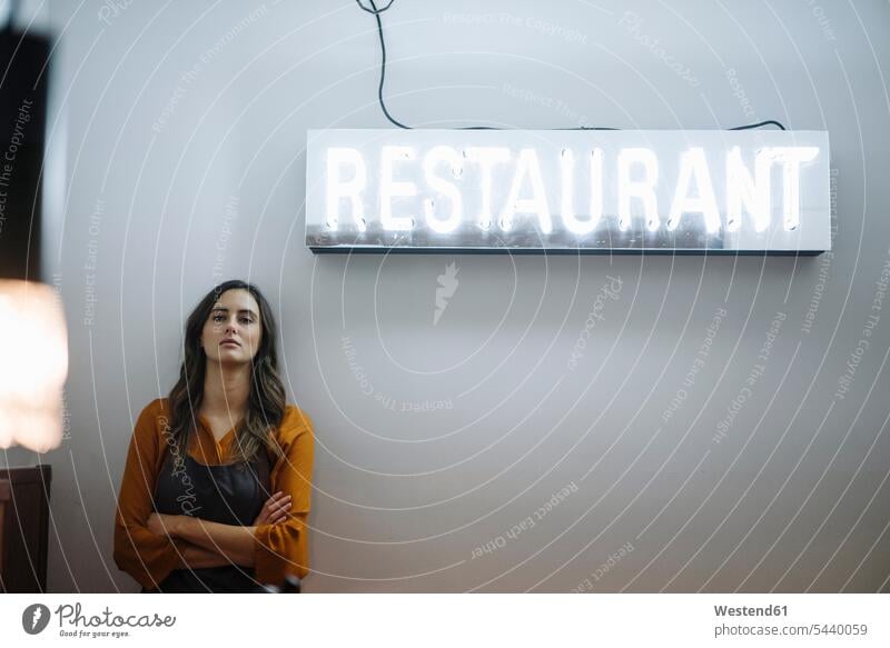 Serious young woman leaning against a wall under restaurant neon light Germany self-employment self-employed One Word Single Word western script