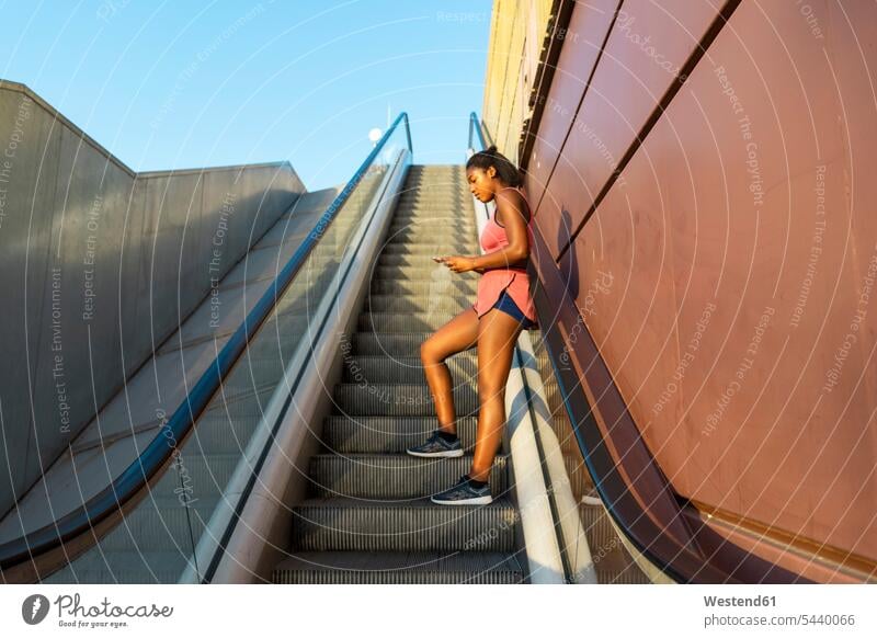 Young sportive woman on escalator using smartphone use moving staircase moving stairs Escalators sporting sporty athletic athlete sportswoman athletes