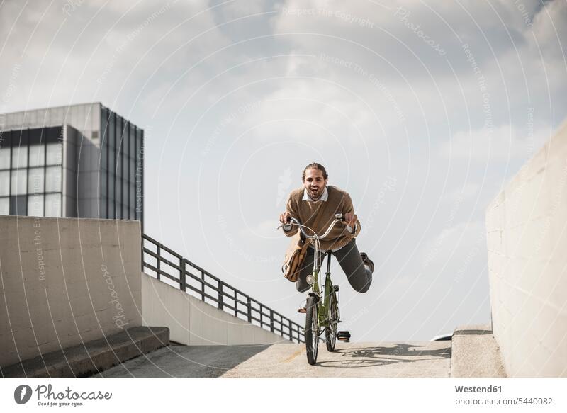 Laughing businessman riding down a ramp on his bicycle young downhill Fun having fun funny fast quick speediness rapidity rapidness apace laughing Laughter