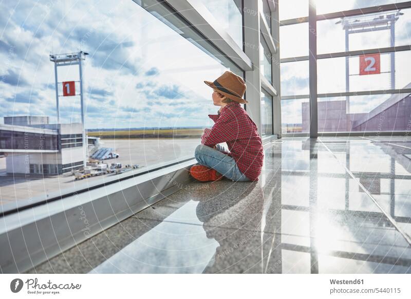 Boy sitting behind windowpane at the airport looking at airfield window glass window glasses windowpanes Window Pane windows airports Seated boy boys males view