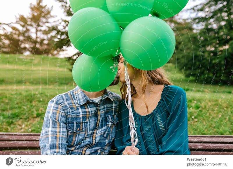 Young couple kissing behind green balloons twosomes partnership couples kisses people persons human being humans human beings hiding hide colour colours Hide