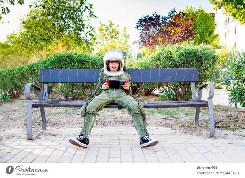 Boy wearing a space suit and sitting on a bench, using tablet human human being human beings humans person persons caucasian appearance caucasian ethnicity