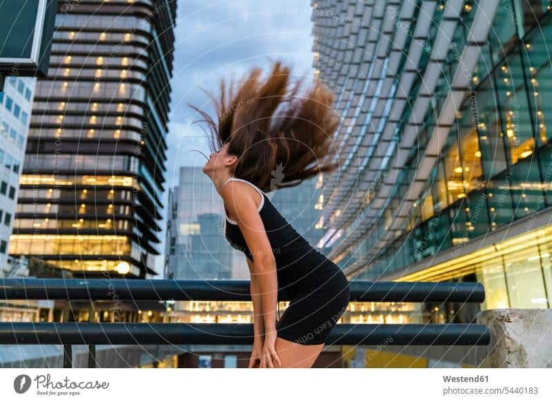 Carefree young woman wearing black dress in the city at dusk tossing her hair females women carefree town cities towns atmosphere atmospheric evening