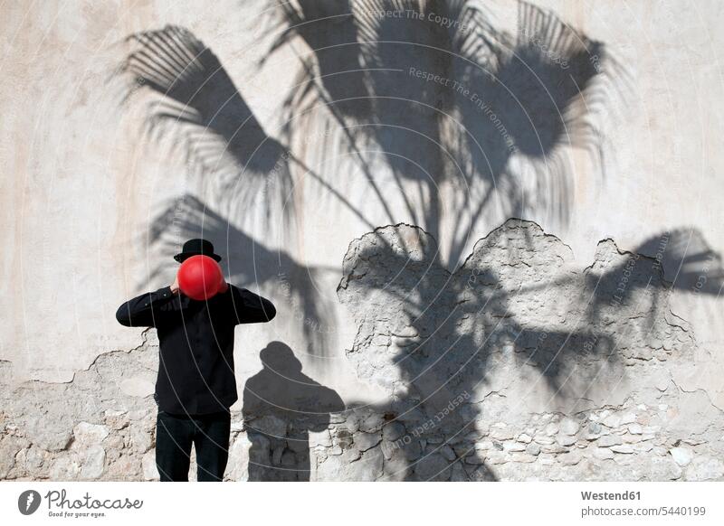 Morocco, Essaouira, man wearing a bowler hat holding red balloon in front of his face at a wall men males balloons colour colours hats Adults grown-ups grownups