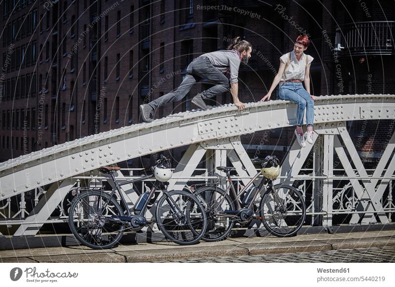Germany, Hamburg, couple with electric bicycles having fun on a bridge twosomes partnership couples E-Bike Electric bicycle Electric Bike people persons