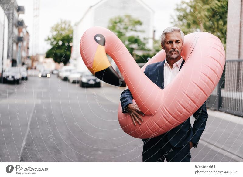 Mature businessman on the street with inflatable flamingo Businessman Business man Businessmen Business men flamingos business people businesspeople