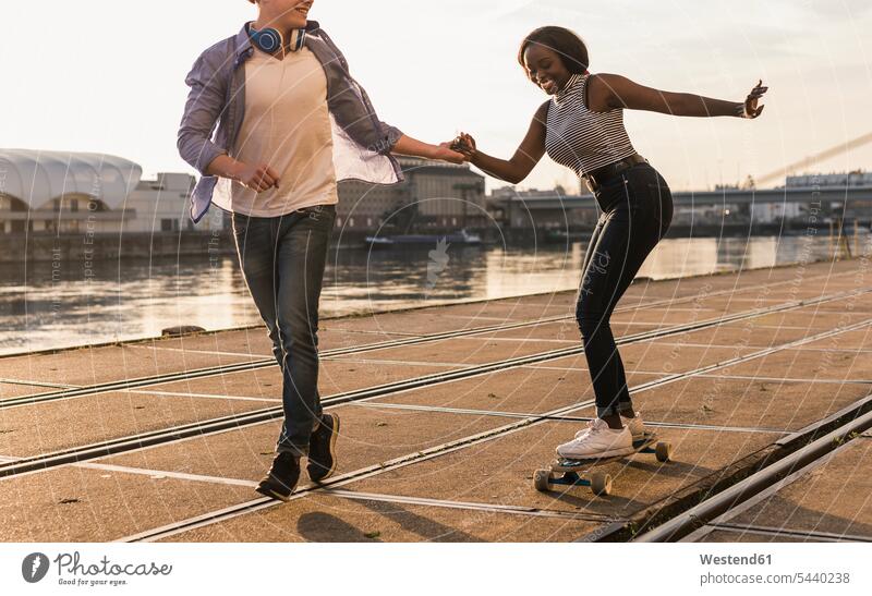 Young couple skateboarding at the riverside multicultural Boarding pulling holding hands hand in hand cheerful gaiety Joyous glad Cheerfulness exhilaration