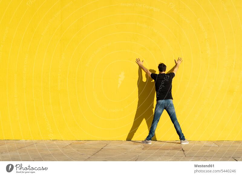 Man standing with hands on yellow wall, rear view leaning walls man men males back view view from the back Adults grown-ups grownups adult people persons
