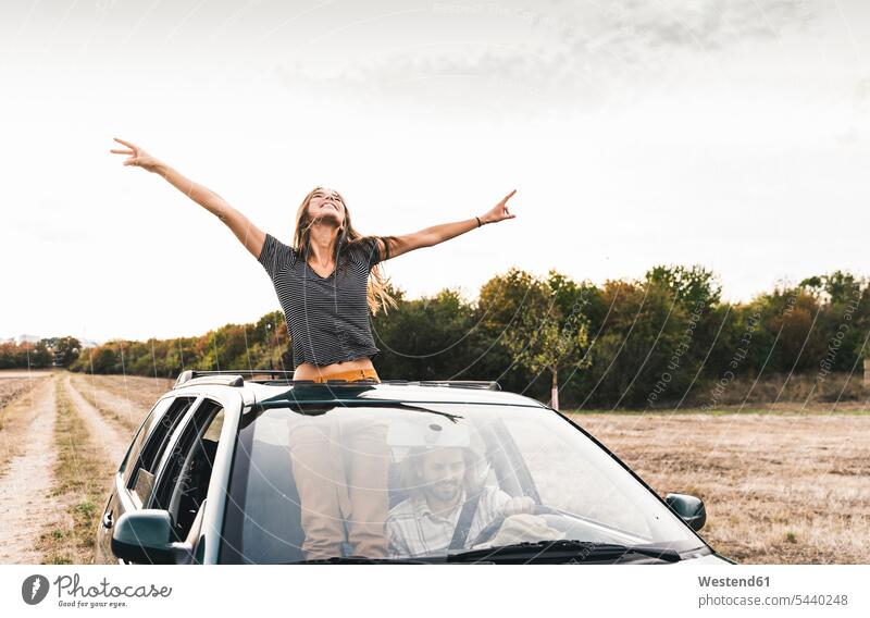 Carefree young woman looking out of sunroof of a car automobile Auto cars motorcars Automobiles females women carefree motor vehicle road vehicle road vehicles