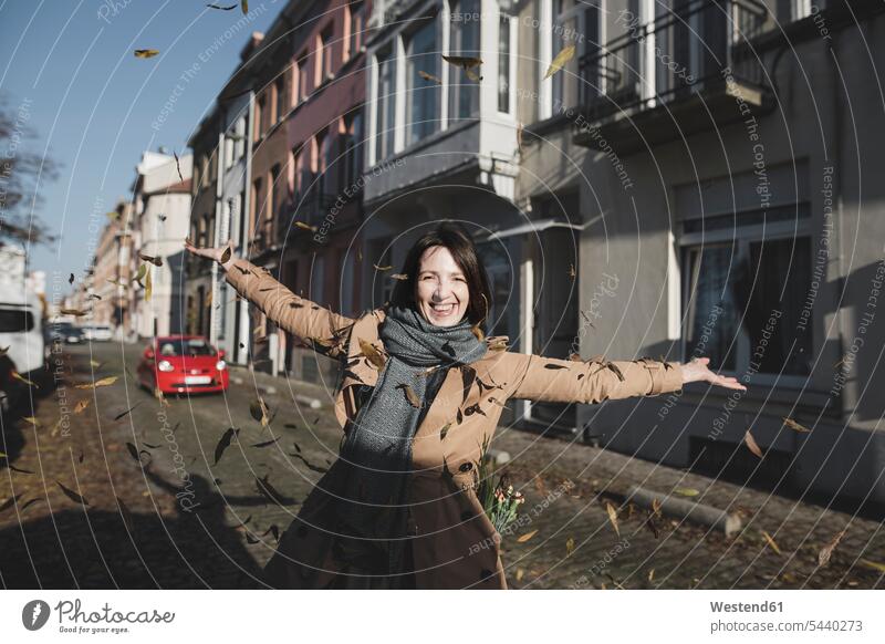 Belgium, Brussels, portrait of happy woman throwing autumn leaves in the air females women portraits happiness autumn leaf Adults grown-ups grownups adult