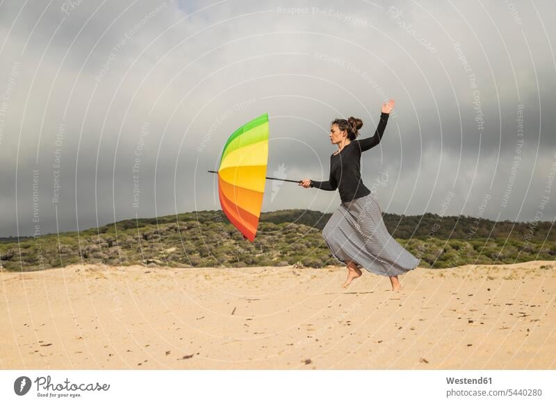 Woman holding colorful umbrella on a dune woman females women fighting sunshade sunshades nonconformist unadapted nonconformity beach dune beach dunes