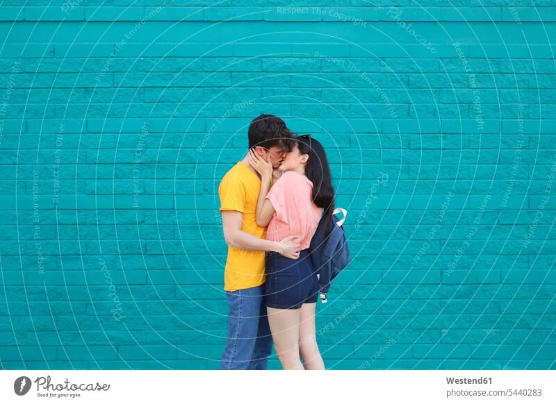 Young couple kissing in front of blue brick wall kisses lovers twosomes partnership couples people persons human being humans human beings standing in love