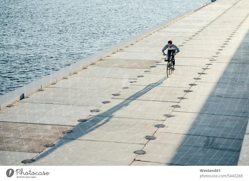 Young man riding bike on waterfront promenade at the riverside bicycle bikes bicycles River Rivers riverbank males transportation promenades waters