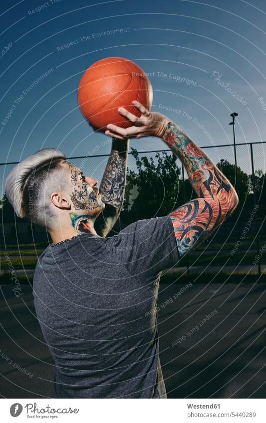 Tattooed young man throwing basketball on outdoor court tattooed tattoos sports field sports fields men males basketballs body art Body Adornment Skin Art style