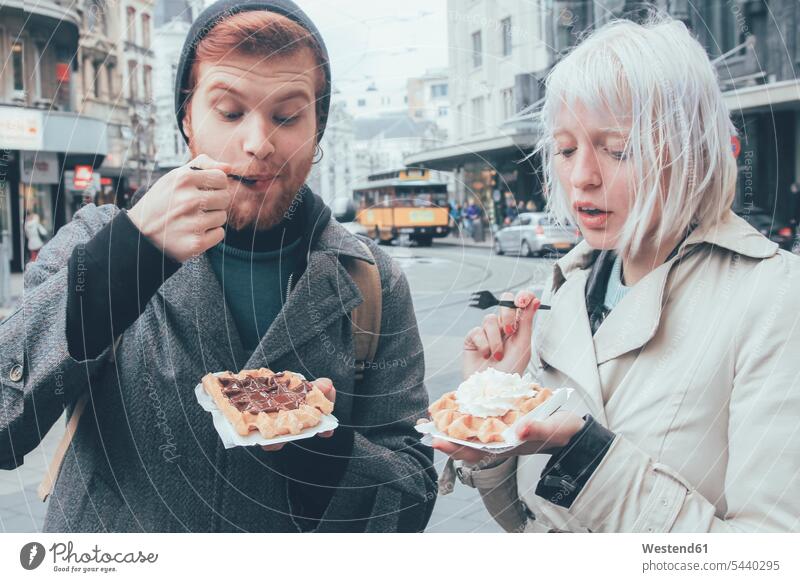 Belgium, Antwerp, young couple eating Belgian waffles on the street streets City Street City Streets unconventional Offbeat whipped cream dairy cream
