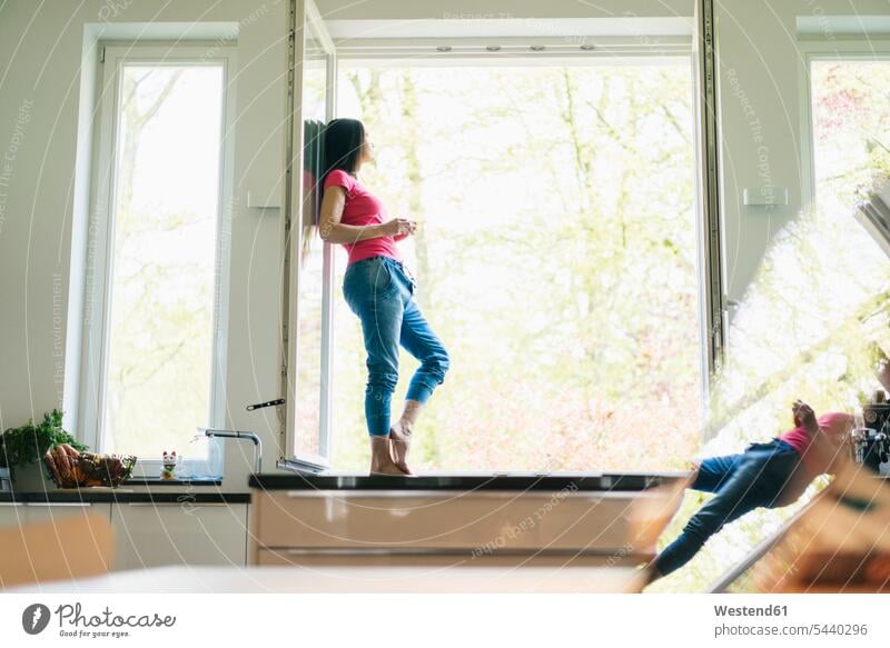 Woman standing in kitchen on windowsill woman females women Adults grown-ups grownups adult people persons human being humans human beings home at home casual