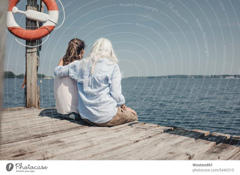 Mother and daughter looking at the sea, sitting on jetty, rear view human human being human beings humans person persons caucasian appearance