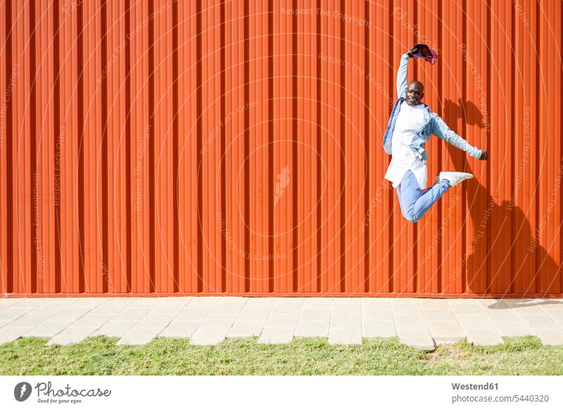 Man wearing casual denim clothes jumping in the air in front of orange wall jeans Denim Jeans jump in the air clothing walls Leaping trousers pants Trouser