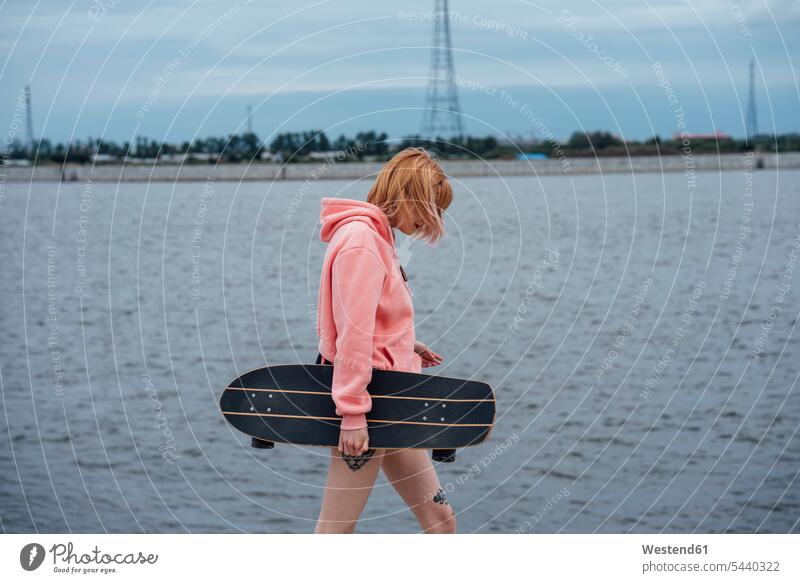 Young woman holding carver skateboard walking at the riverside riverbank Skate Board skateboards River Rivers females women going water's edge waterside shore