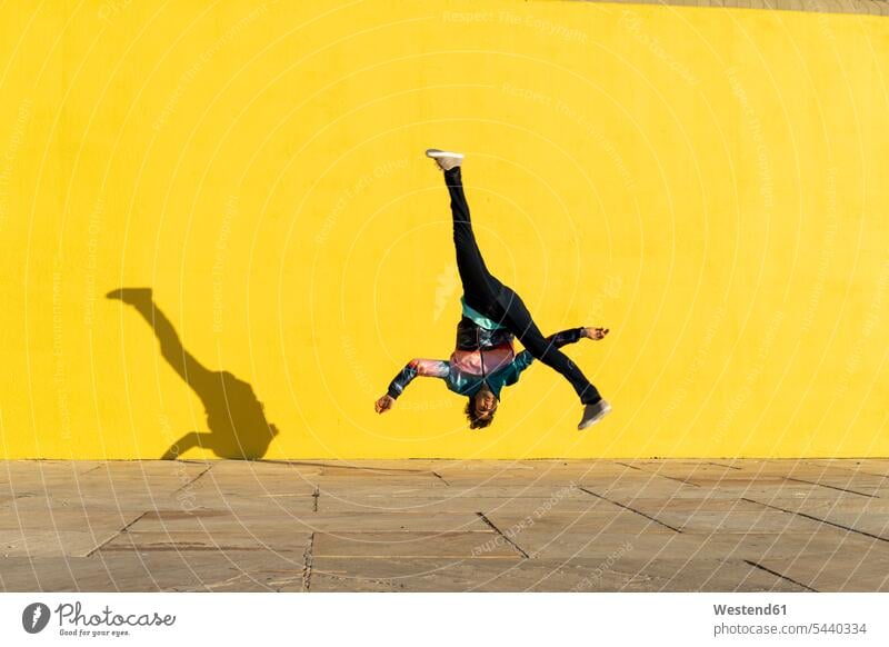 Acrobat jumping somersaults in front of yellow wall Somersaulting Flip acrobat acrobats equilibrists walls Leaping acrobatics Acrobatic Activity sport sports