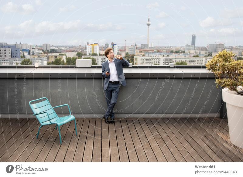 Germany, Berlin, businessman having a drink on roof terrace after work Businessman Business man Businessmen Business men deck rooftop After Work afterwork Drink
