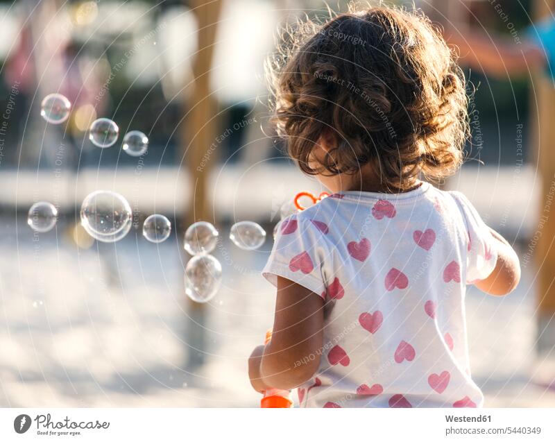 Back view of little girl making soap bubbles at playground caucasian european caucasian ethnicity caucasian appearance day daytime daylight shot day shots