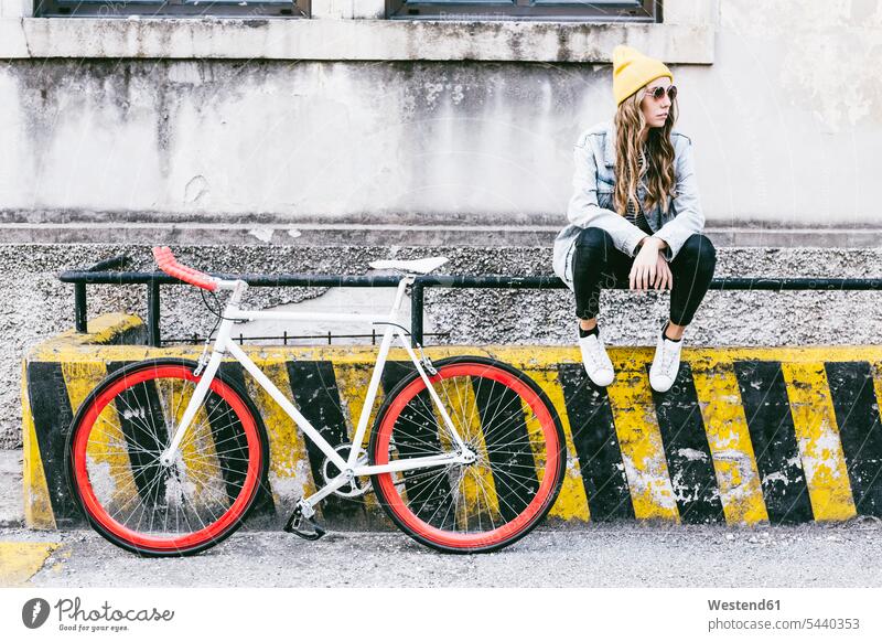 Fashionable young woman with bicycle sitting on railing Seated Railing Railings fashionable bikes bicycles females women Adults grown-ups grownups adult people