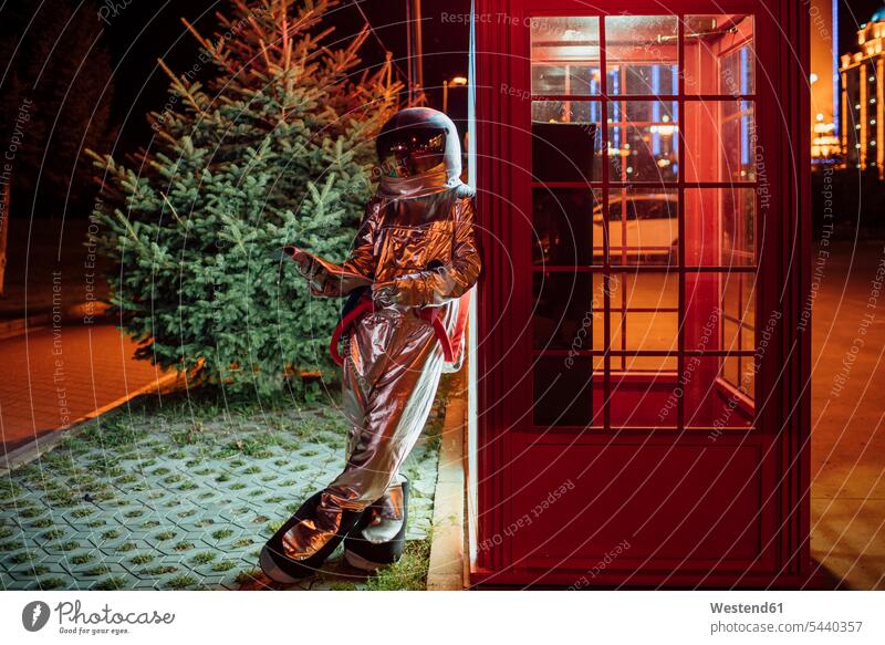 Spaceman leaning against a telephone box at night reading phone book astronaut astronauts telephone booth telephone kiosk callbox spaceman spacemen standing