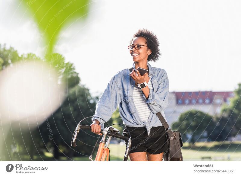 Smiling young woman with cell phone and bicycle in park bikes bicycles mobile phone mobiles mobile phones Cellphone cell phones parks females women smiling