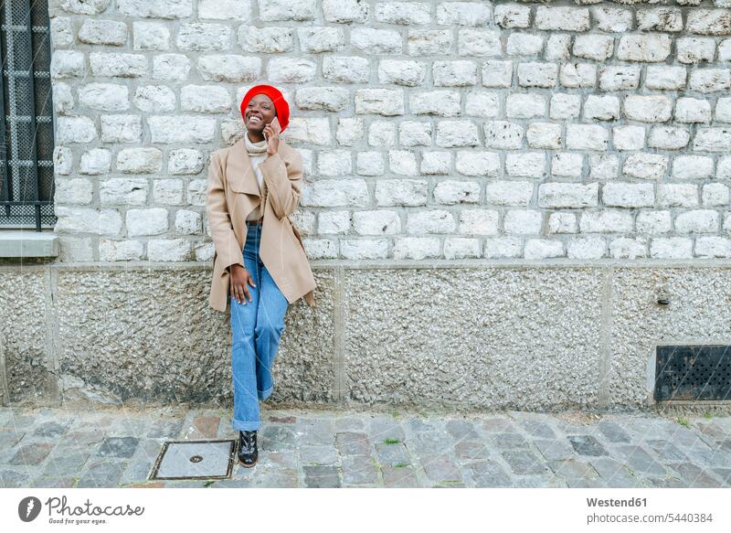 Young woman in Paris leaning against wall and talking on the phone females women Smartphone iPhone Smartphones call telephoning On The Telephone calling smiling